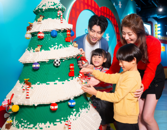 A group of people and a child playing with a lego christmas tree

Description automatically generated